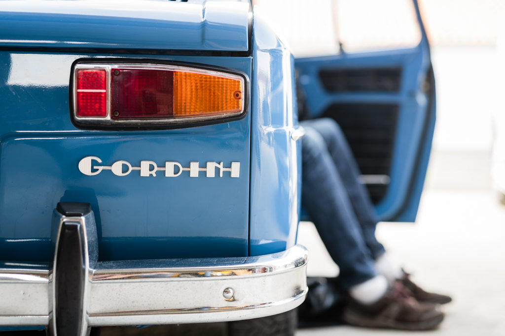 feu arrière d'une R8 gordini bleue, avec une personne en jean dont les jambes dépassent côté passager.