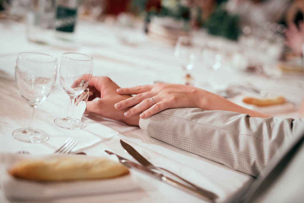 détail des mains des mariés pendant le repas. La main de la mariée, avec l'alliance, est posée sur celle de son mari.