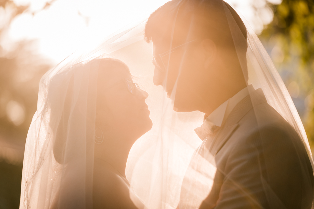 Couple se regardant dans les yeux sous un voile de mariée à l'heure dorée