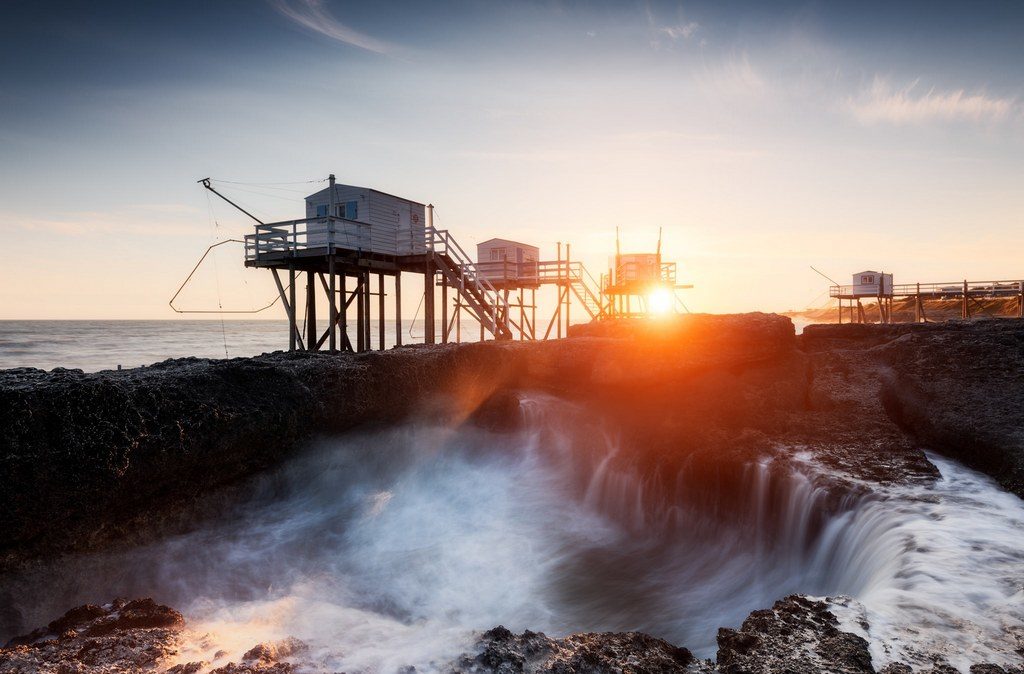 Vague passant par un trou dans la roche, et coucer de soleil sur les carrelets