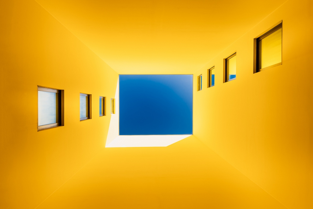 Bâtiment jaune en contre-plongée avec un carré de ciel bleu se détachant au centre de l'image