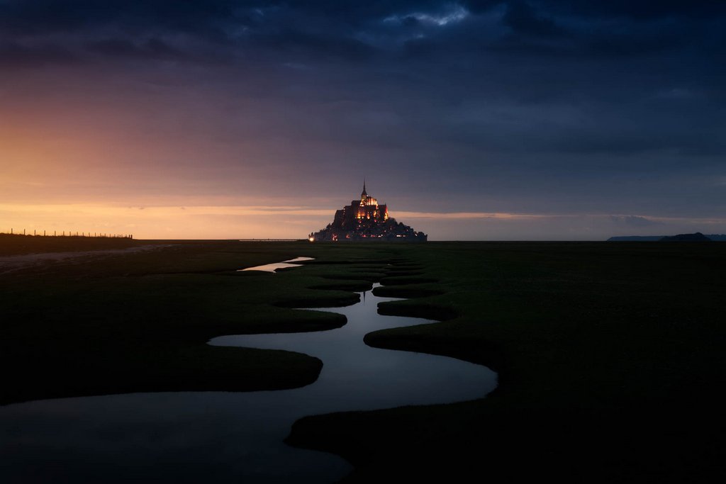 Mont Saint Michel at sunset. Meanders in the foreground direct the gaze towards the mountain, in the center of the image in the background