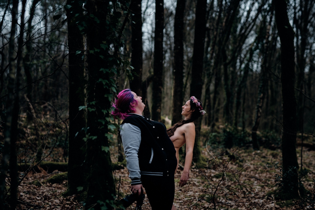 Photographe pendant une séance de nu en forêt, montrant au modèle la position à adopter