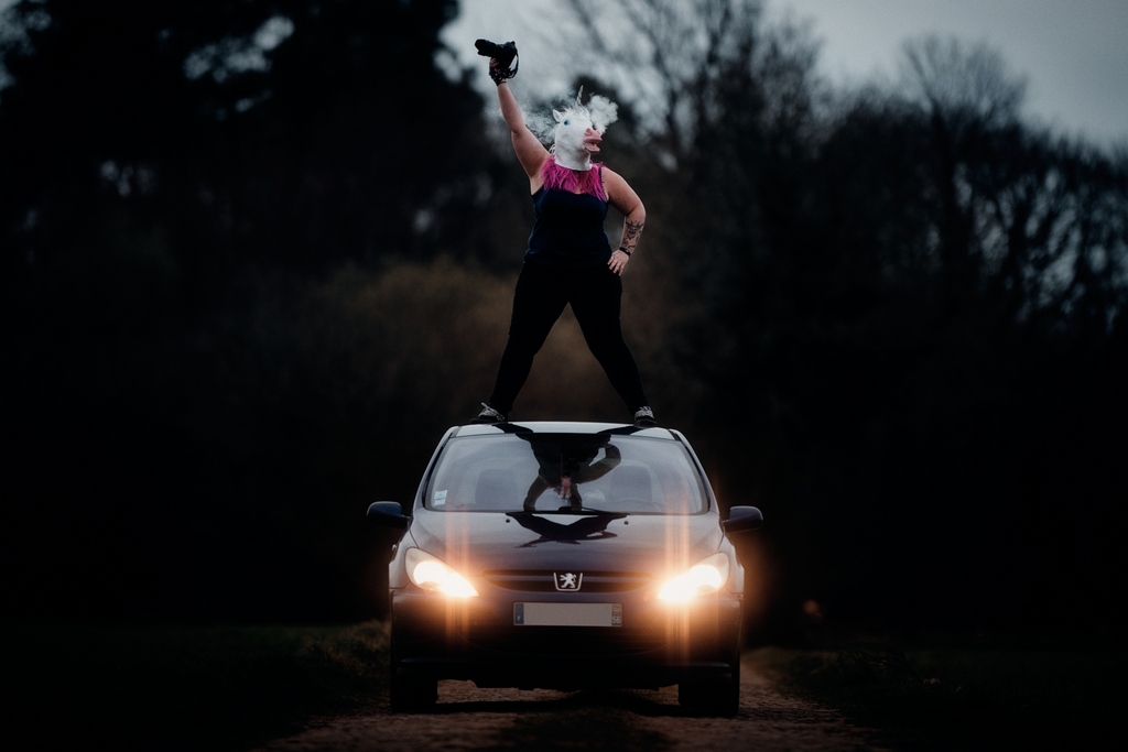 Portrait professionnel d'une photographe de mariage décalée : la photographe se tient sur le toit de sa voiture avec un masque de licorne
