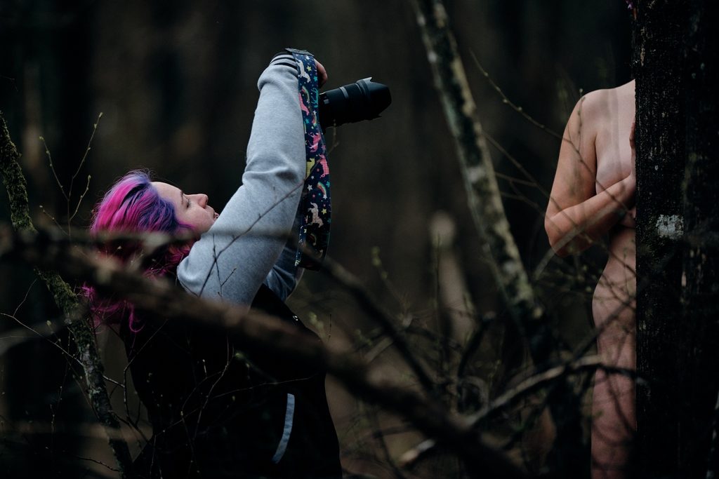 Photographe prenant en photo une modèle que l'on devine entre deux arbres
