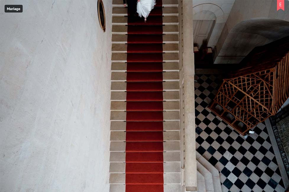 Couple de mariés descendant l'escalier de la mairie de Bourges, décoré d'un tapis rouge avec un damier au sol 