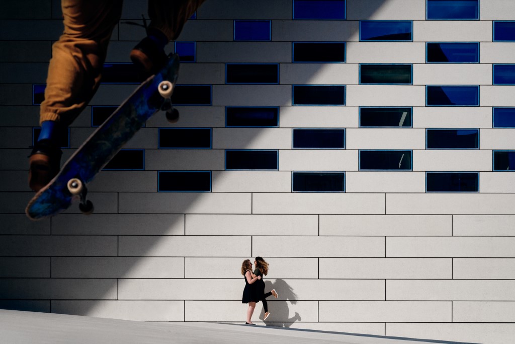 Couple de femmes s'embrassant devant un mur tandis qu'un skate passe devant