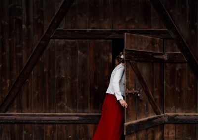 Photo d'une invitée de mariage près de Strasbourg vêtue d'une robe rouge et d'une veste blanche entrant dans la grange où se passe le mariage