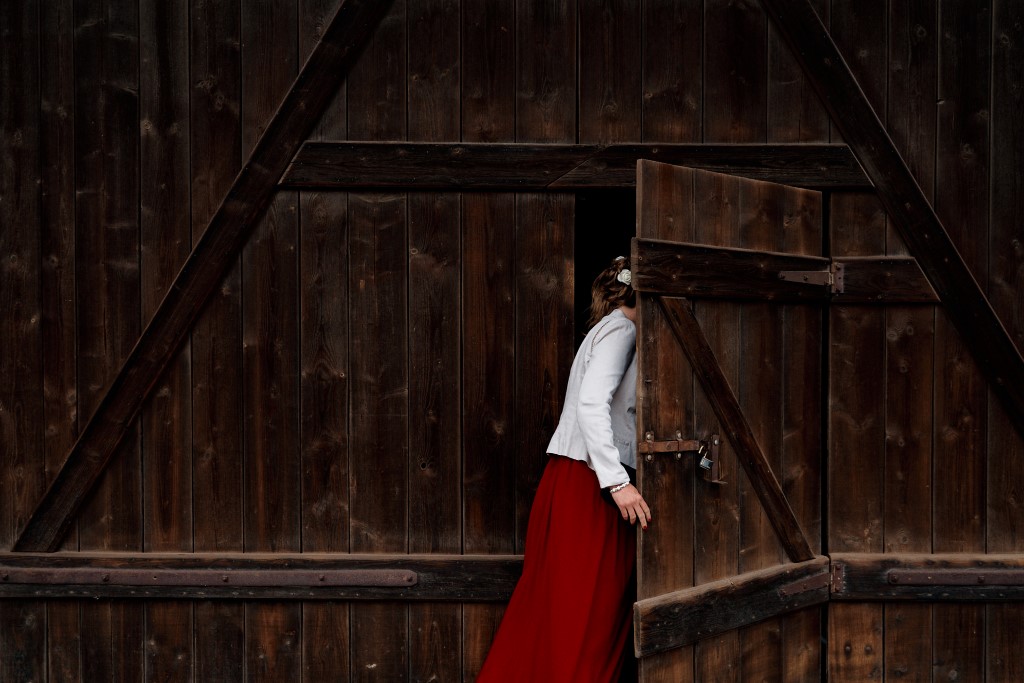 Photo d'une invitée de mariage près de Strasbourg vêtue d'une robe rouge et d'une veste blanche entrant dans la grange où se passe le mariage