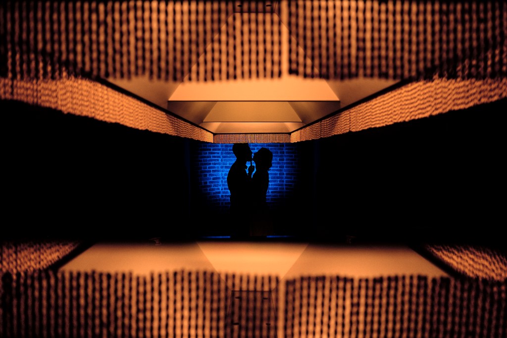 Photo prise par un photographe de mariage à Lyon grâce aux éclairages d'une table de billard. La silhouette du couple se détache au fond sur un cercle bleu, et deux bandes jaunes encadrent le couple en haut et en bas