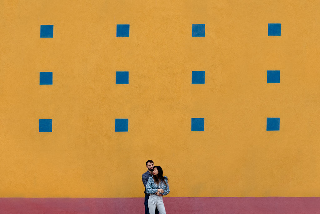 Love session en milieu urbain, un couple devant un mur jaune et rouge avec des carrés bleus