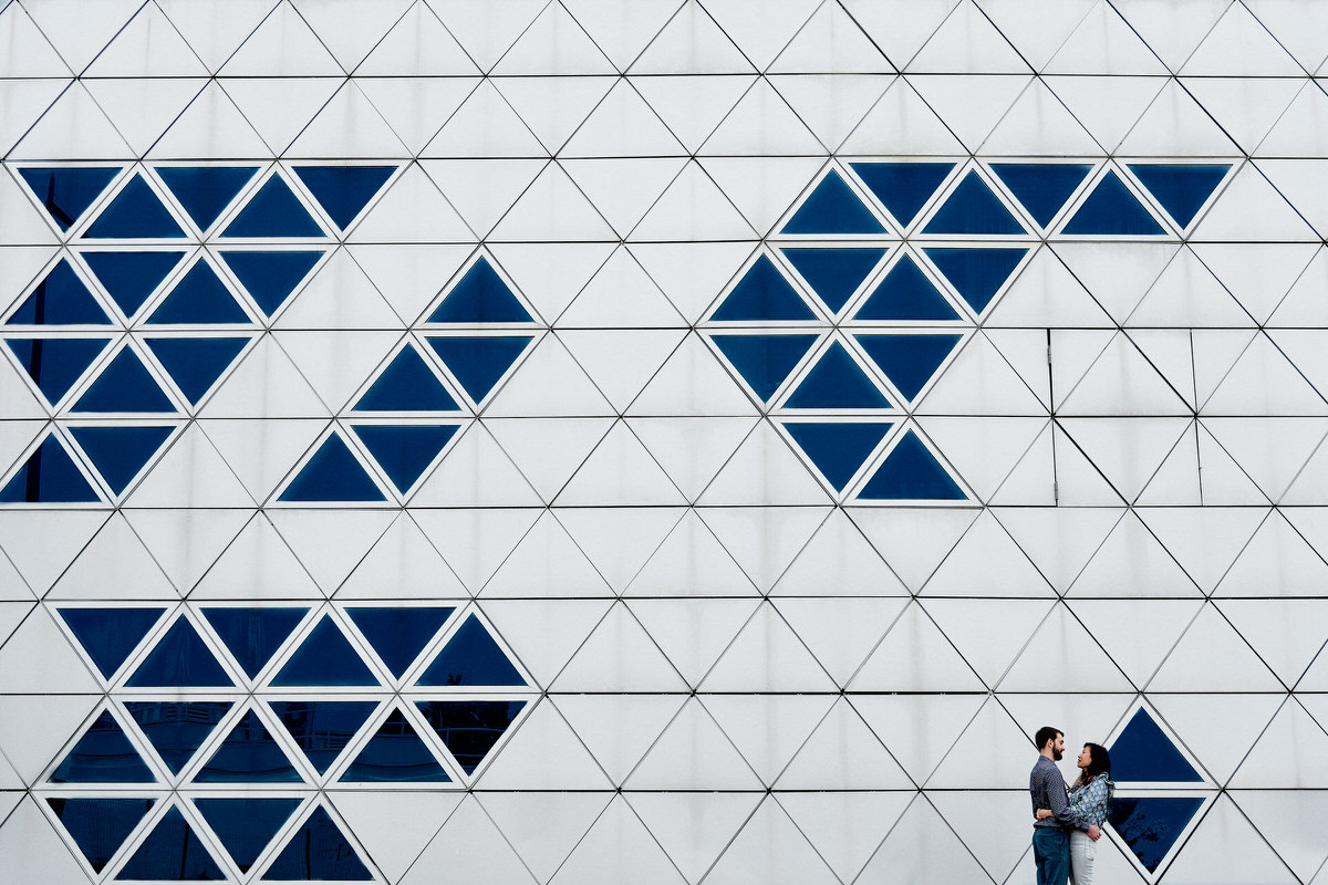 photo de couple devant une façade de bâtiment graphique composée de triangles blancs et bleus