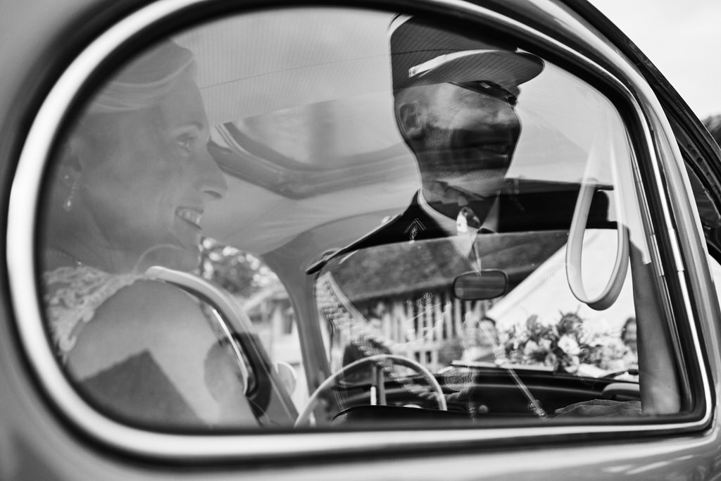 Couple de mariés se rendant à l'Eglise. La mariée souriante à travers la fenêtre, le marié souriant dans le reflet de la fenêtre. Tous les deux regardant dans la même direction.